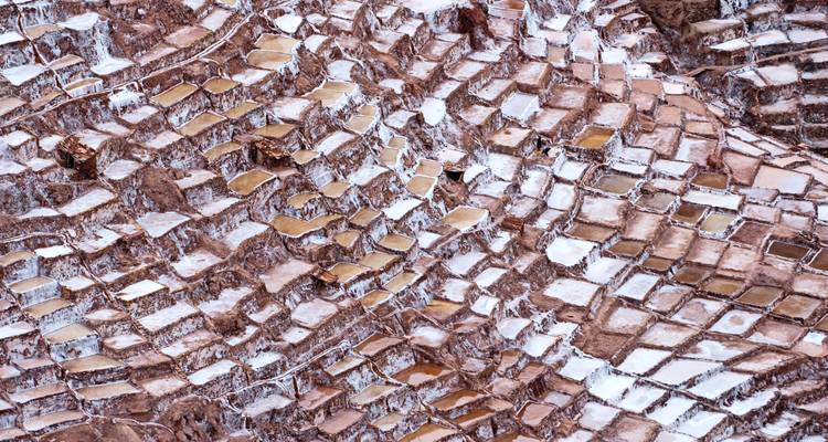 Abstrakte Luftaufnahme eines gestaffelten Musters von Salzbecken mit weißen Mineralablagerungen in rosa-braunem Erdreich.