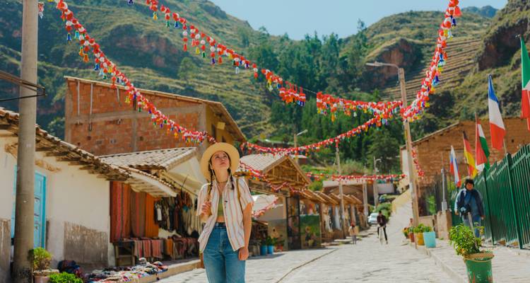 Un jeune voyageur coiffé d'un chapeau marche dans une rue festive d'un village andin décorée de guirlandes de fanions colorés entre des boutiques en adobe.