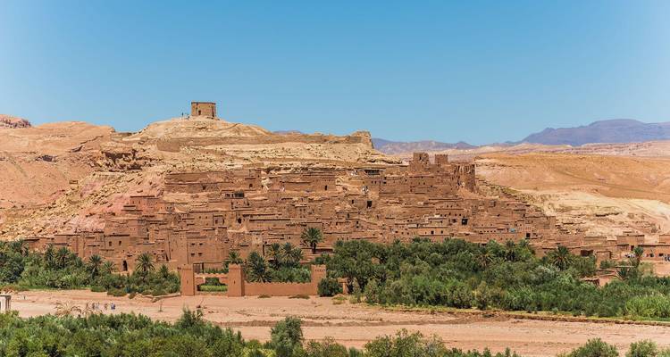 Vista panorámica del ksar de tierra de Ait Benhaddou respaldado por colinas áridas y vegetación.