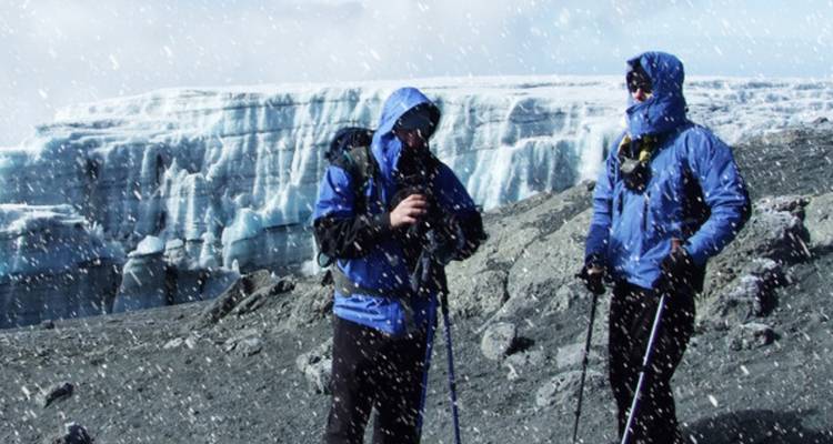Deux trekkeurs vêtus de vestes bleues se tenant debout dans les chutes de neige près du glacier de cratère du Kilimandjaro