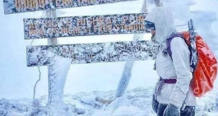 Alpiniste équipé à côté d'un panneau du pic Uhuru recouvert de glace dans des chutes de neige abondantes