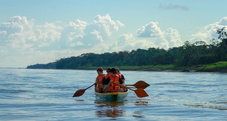 Quatre voyageurs pagayant un canoë sur un large fleuve tropical avec une toile de fond de jungle.