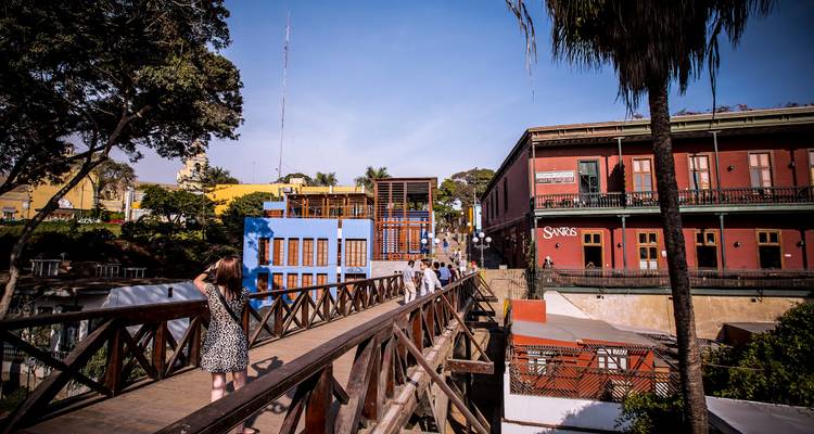 Visitors cross the wooden Bridge of Sighs in Lima’s Barranco district surrounded by colourful colonial buildings under a clear sky.