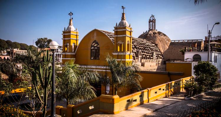 Bright yellow colonial church with twin white bell towers surrounded by palm trees in Lima’s Barranco neighbourhood.