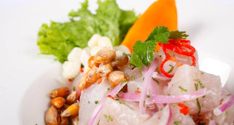 Close-up of fresh Peruvian ceviche garnished with red onion, cilantro, cancha corn and sweet potato on a white plate.
