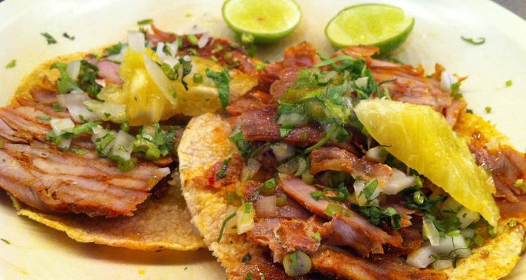 Nahaufnahme von zwei gefüllten Tacos mit Ananas und Koriander auf einem schlichten Teller