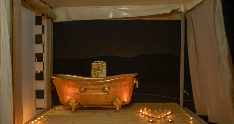 Bañera de cobre al aire libre con luz de velas en una terraza de madera mirando hacia la noche oscura del desierto.