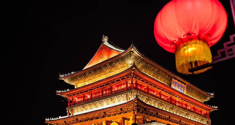 Close-up of Xi’an Drum Tower illuminated beside a vivid red lantern against the black night sky.
