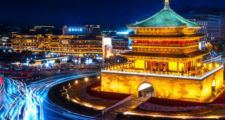 Night view of Xi’an Bell Tower illuminated in gold with dynamic light trails from passing traffic.