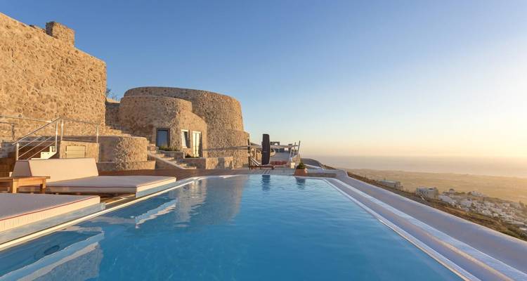 Une piscine à débordement et une villa en pierre offrent une vue sur la mer Égée au lever du soleil à Santorin.