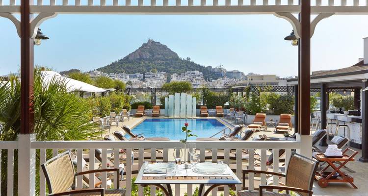 Terrasse de la piscine de l'hôtel avec vue sur la colline du Lycabette surplombant Athènes sous un ciel dégagé.