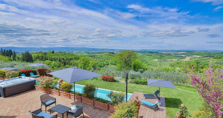 Terras met zwembad, zonnebedden en parasols met uitzicht op het uitgestrekte groene Toscaanse platteland.