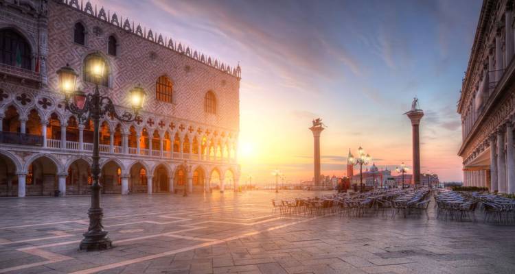 Zonsopganglicht vult het Piazza San Marco met het Doge's Palace en lege cafestoelen.