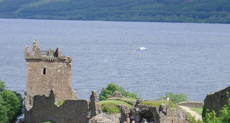 Ruines du château d'Urquhart sur la rive d'un vaste loch avec des collines boisées au-delà.