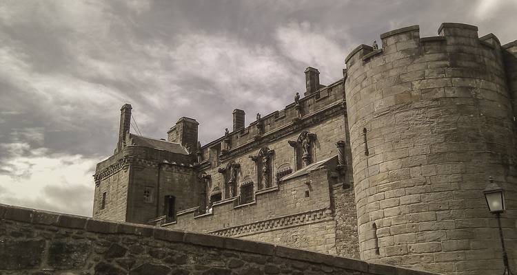 Les murs de pierre austères et les tours imposantes d'un château médiéval majestueux sous des nuages dramatiques.