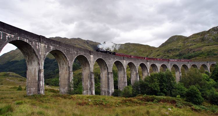 Train à vapeur traversant les arches élancées du Viaduc de Glenfinnan au milieu de collines verdoyantes luxuriantes.