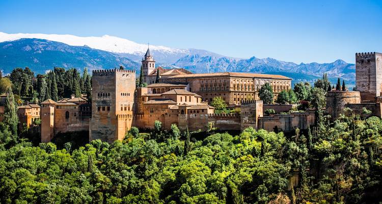 Die ikonische Alhambra-Festung, umgeben von grünem Wald vor einer Kulisse schneebedeckter Berge.