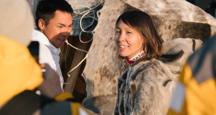 Inuit-Gastgeber lächeln während einer kulturellen Begegnung und tragen traditionelle Pelzkleidung.