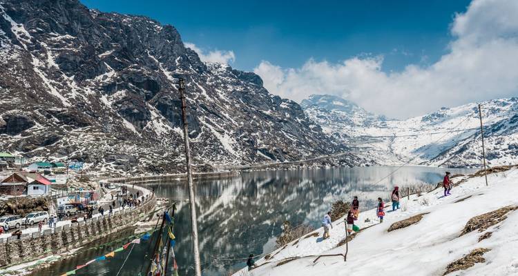 Snow-capped mountains reflected in the crystal waters of Tsomgo Lake with prayer flags fluttering