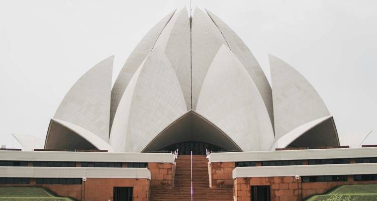 Moderner weißer Lotus-Tempel mit blütenblattartiger Architektur vor einem bewölkten Himmel.