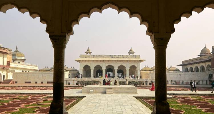 Ein Mogul-Hof, umrahmt von kunstvollen Bögen, die zu einer Halle aus weißem Marmor mit Besuchern führen.