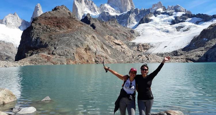 Two hikers celebrate beside turquoise Laguna de los Tres backed by Fitz Roy’s spires and glacier.