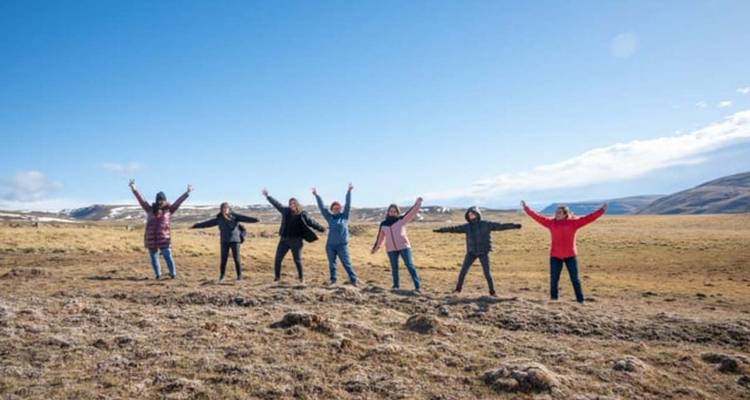 Seven travellers spread arms wide on an open Patagonian plain beneath blue sky.