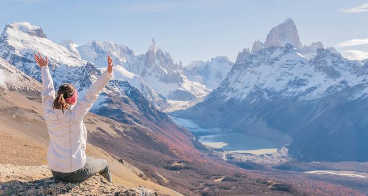 Traveller with raised arms admires panoramic snow-capped Fitz Roy range and valleys below.