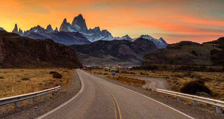 Open road leading toward jagged Mount Fitz Roy at sunset with vivid sky hues.