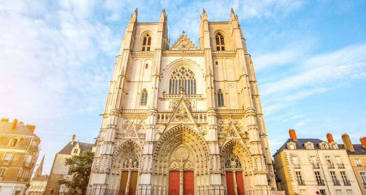 A soaring Gothic cathedral façade glows in warm morning light against a soft blue sky.