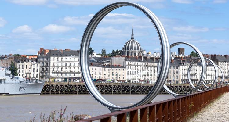 Modern art installation of giant metal rings along the Loire River with Nantes’ skyline behind.