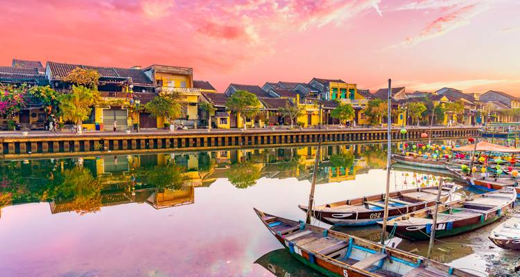 Historische winkelhuizen en kleurrijke boten spiegelen zich in een rustig kanaal onder een levendige roze zonsonderganghemel.