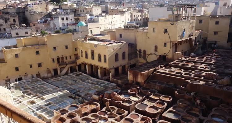 Draufsicht auf traditionelle Gerbereibottiche in Fes, gefüllt mit farbigen Flüssigkeiten neben gelben Gebäuden.