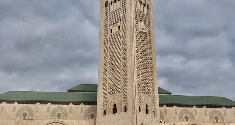 Nahaufnahme des kunstvollen Minaretts der Hassan-II.-Moschee, das sich in einen bewölkten Himmel erhebt.