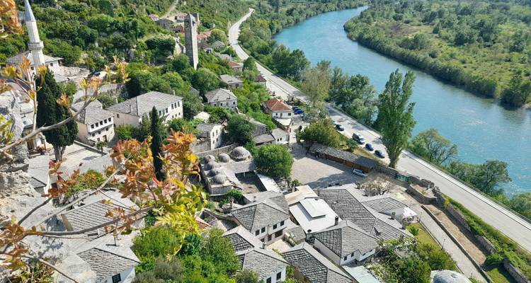 Una vista aérea de las casas con techos de piedra y las cúpulas de la mezquita del pueblo de Počitelj junto a un río de color turquesa.