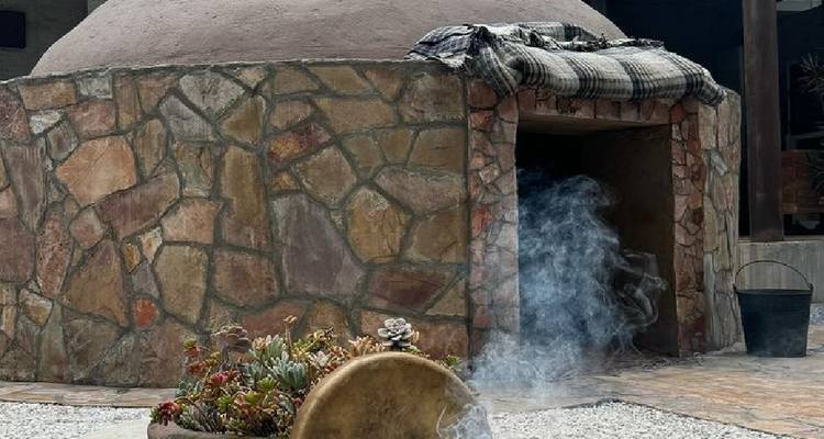 Steinstruktur eines Temazcal mit Rauchentwicklung neben einem Innenhof mit weißem Kies.