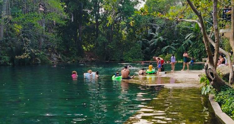 Natürlicher Smaragd-Quellpool, beschattet durch Dschungelbäume, mit Badegästen und Schwimmreifen.