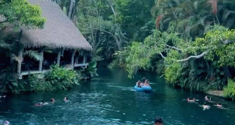 Reetgedecktes Flussufferrestaurant neben einem Dschungelwasserweg, wo Besucher paddeln und schwimmen.