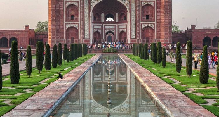 Eingangstor des Taj-Mahal-Komplexes, das sich im langen Marmorbecken widerspiegelt, das von Zypressenbäumen gesäumt ist.