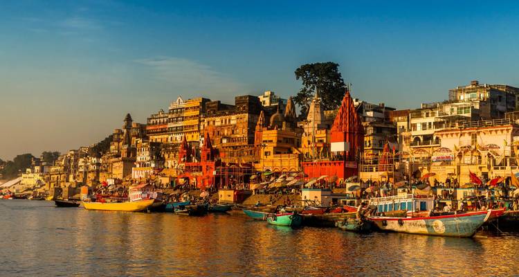 Aussicht zur goldenen Stunde auf die Varanasi-Ghats mit farbenfrohen Tempeln und Booten am Ganges.