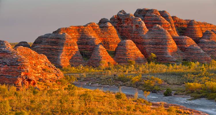 Striking beehive-shaped sandstone domes glow orange in the low light, with a dry creek bed and scrub in the foreground.