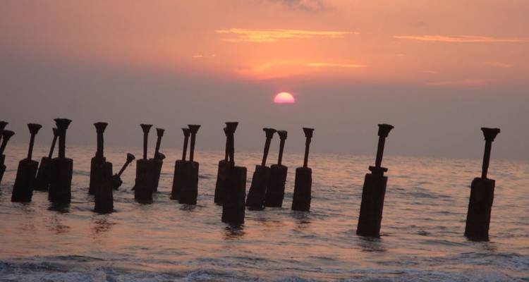Orange Sonne geht über dem ruhigen Meer unter, während sich im Vordergrund Reihen von verwitterten Holzpfählen abzeichnen