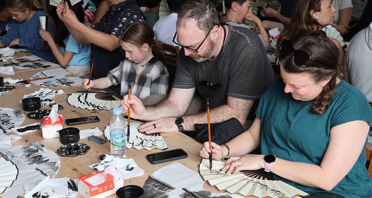 Les voyageurs peignent des éventails en papier traditionnel lors d'un atelier culturel intérieur
