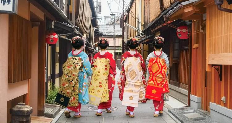 Quatre maiko vêtues de kimonos aux couleurs éclatantes marchent dans une ruelle étroite de Kyoto