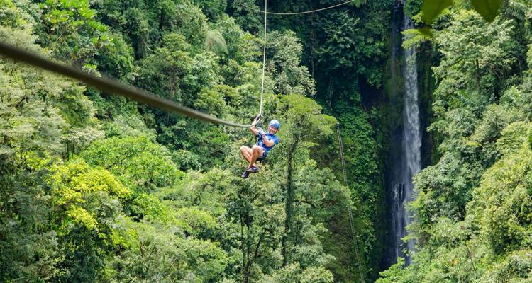 Aventurier pratiquant la tyrolienne au-dessus d'une dense forêt tropicale avec une cascade en arrière-plan