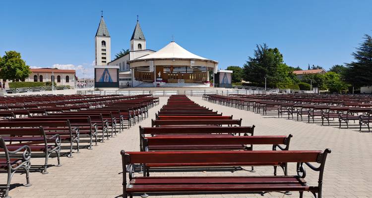 Outdoor seating rows face the twin-tower St. James Church in Medjugorje under clear sky