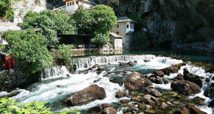 The historic Blagaj Tekke monastery beside a clear river flowing over a small weir and rocks