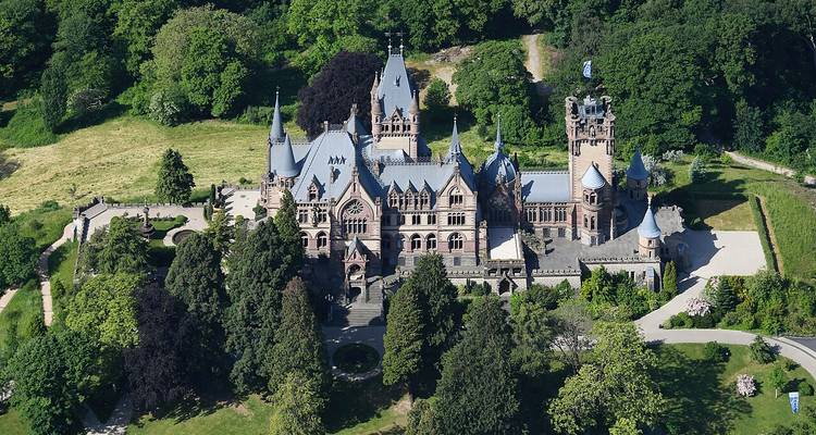 Luchtfoto van het sprookjesachtige Schloss Drachenburg verscholen in een dicht groen bos.