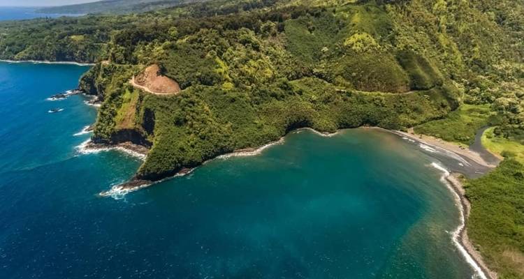 Luchtfoto van ruige groene kliffen en een turquoise baai langs Hawaiis kustlijn.