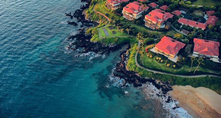 Luchtfoto van zonsondergang met luxe villa's met rode daken gebouwd op een rotsachtige Hawaiiaanse kust.